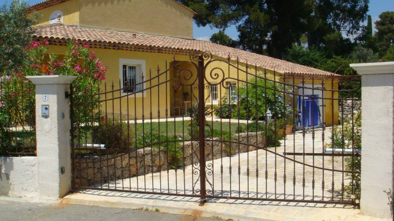 Portail ajouré en fer forgé élégant à Antibes, avec volutes décoratives pour une entrée de maison raffinée.